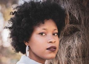 Young Black woman with a natural afro leaning on a palm tree