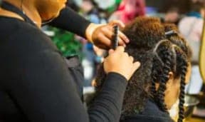 A stylist twisting a Black woman's natural hair
