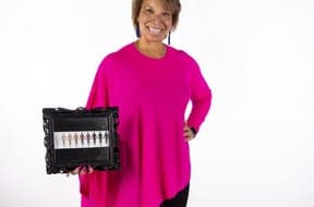 Smiling Black woman in a pink top holding a framed skin-tone scale