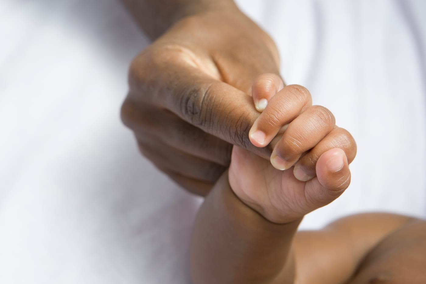 An infant’s hand holding an adult’s finger.