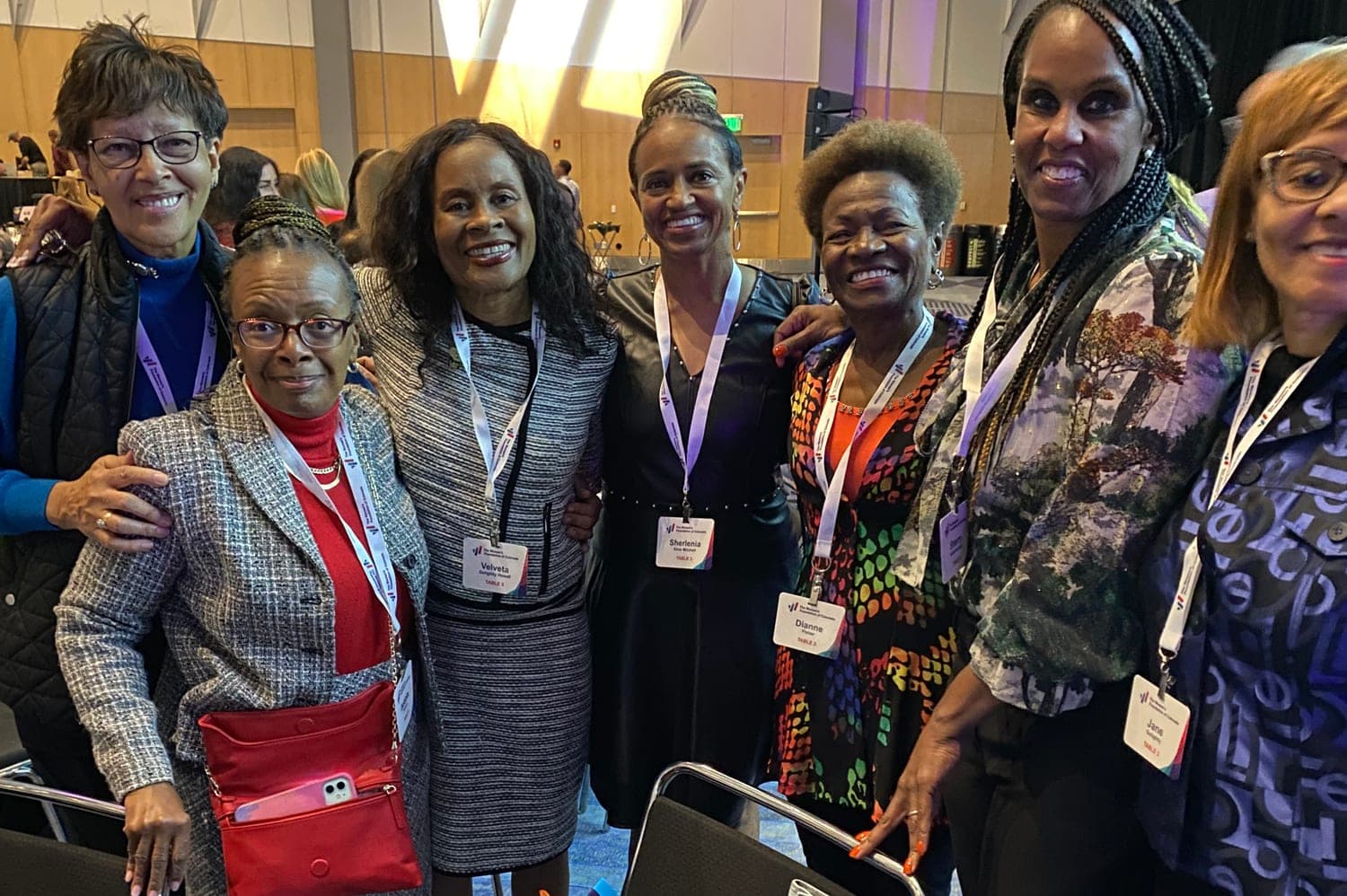 Seven Sister-to-Sister members with event lanyards, smiling together at a luncheon